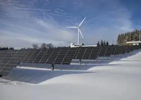 Solar panels and wind turbine in a snowy landscape, showcasing renewable energy sources.