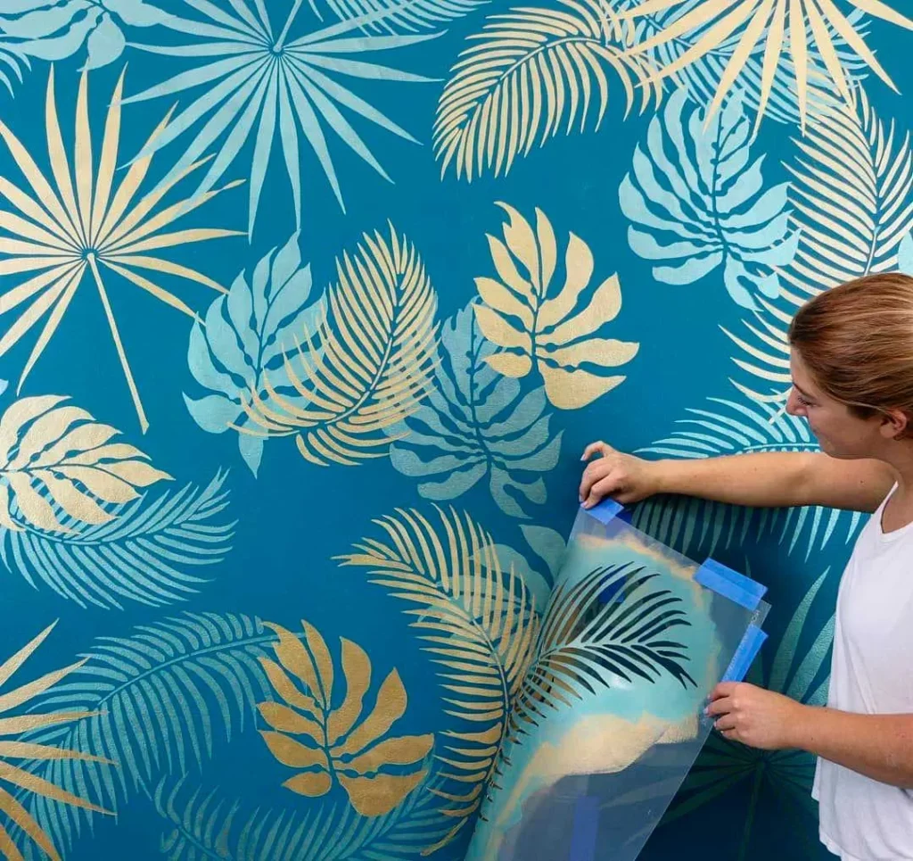 Mujer decorando pared azul con plantilla de hojas tropicales