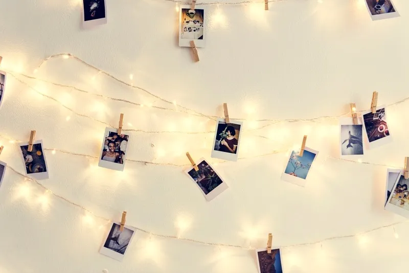 Fotografías colgadas con pinzas sobre luces LED en pared blanca